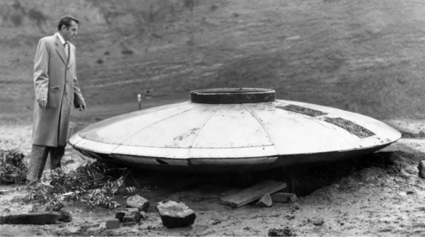Black and white photo of Los Angeles Times aviation writer Dewey Linze examines flying saucer found in the Hollywood Hills. Jan. 24, 1957.